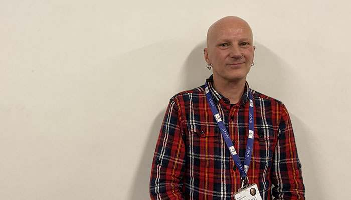 Man in checked shirt standing against cream wall