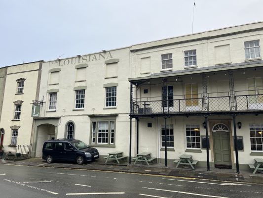 The entrance of The Louisiana, a music venue in Bristol with a car parked in front of it.